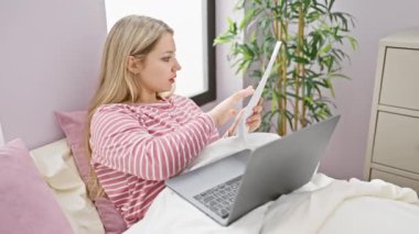 Genç bir kadın, rahat ve modern bir yatak odasında dizüstü bilgisayarı üzerinde çalışırken bir kağıdı analiz eder.