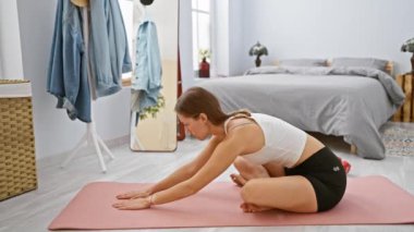 Genç bir kadın yatak odasında yoga yapıyor. Huzurlu bir sağlık ortamı yaratıyor..
