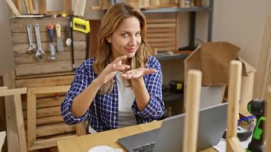 Genç, enerjik Latin bir kadın marangozluk atölyesinde para jesti sergiliyor, gecikmiş maaşı için göz kırparak girişimci başarısını gösteriyor.