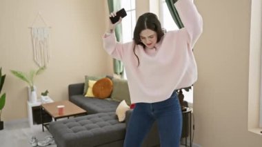 Genç bir kadın modern oturma odasında özgürlüğünü ve mutluluğunu ifade ederek neşeyle tek başına dans ediyor..