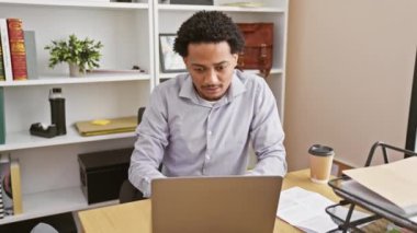 Genç Afro-Amerikan ofis çalışanı masada oturan ağzı şokla kapatıyor. Yüzü, iş yerinde gizlice yapılan kötü bir hatadan sonra şaşkınlık dolu bir sessizlik gösteriyor.