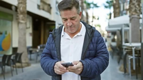 在有室外咖啡馆背景的城市街道上使用智能手机的成熟男人 唤起了城市的交流和生活方式 — 图库视频影像