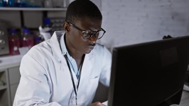 Soustředěný Africký Muž Laboratoři Brýlemi Bílým Kabátem Pracuje Upřeně Počítači — Stock video