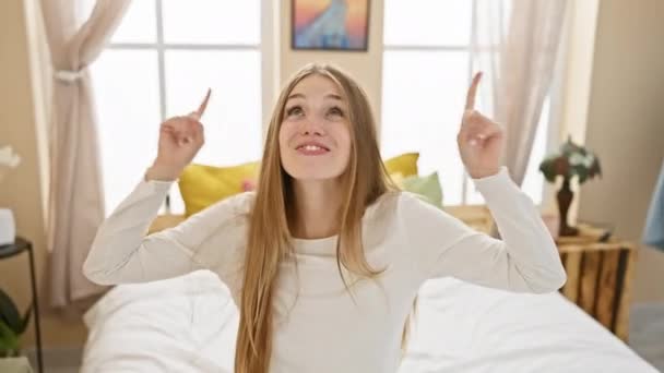 Radosna Młoda Blondynka Siedzi Łóżku Piżamie Uśmiechając Się Zaskoczeniem Wskazując — Wideo stockowe