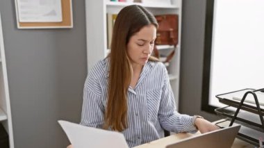 Gözlüklü odaklı bir iş kadını modern ofis ortamında, profesyonelliği ve konsantrasyonu somutlaştıran belgelerle dikkatle çalışır..