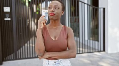 Güzel bir Afro-Amerikan kadını, yüzünde şüpheli bir ifade, açık bir şehir caddesinde duruyor, dolarları ve parayı tutuyor, finans, yatırım ve ekonomiyi düşünüyor..