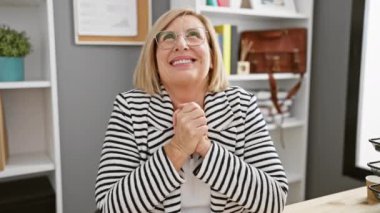 Işıl ışıl orta yaşlı sarışın iş kadını zaferi coşkuyla kutluyor, gülüşü zaferi haykırıyor, ifadesi ofiste neşe saçıyor..