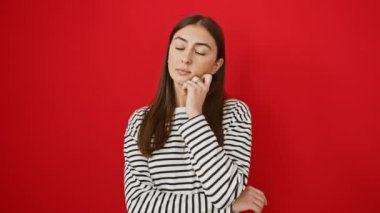 Çizgili tişört giyen genç ve güzel bir İspanyol kadın şüphe üzerine yoğunlaşmıştı. Parmakları çenesinde ve yukarıdan izole edilmiş kırmızı arka planı araştırıyordu.