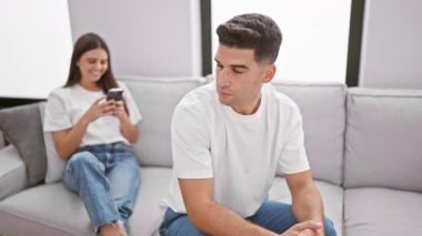 Akıllı telefonlarıyla meşgul olan bir adam ve kadın modern oturma odasındaki rahat bir kanepede ayrı ayrı oturuyorlar.