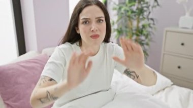 Güzel bir genç kadın, pijama giyiyor, yatak odasında oturuyor, elleri göğsünde, gülümsüyor, minnettarlık jesti, sağlıklı bir yaşam tarzı..
