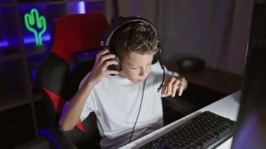 Sevimli sarışın erkek striptizci, fütüristik bir video oyunu oynamaya dalmış, gece dijital oyun odasından teknolojik aletler kullanarak canlı yayın yapıyor, yüzü odaklanmış ama rahat.