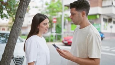 Güneşli bir şehir sokağında akıllı bir telefonla meşgul olan mutlu bir çift.