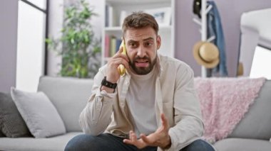 Evdeki oturma odasındaki kanepede oturmuş akıllı telefonuyla tartışan sinirli, genç bir İspanyol.