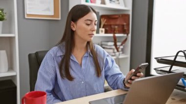 Modern ofis ortamında dizüstü bilgisayarla çalışan İspanyol kadın akıllı telefon kullanıyor..
