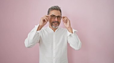 Neşeli genç İspanyol adam gözlüğünü çıkarıyor, gri saçlı ve kendinden emin. İzole edilmiş pembe arka planda ışıldıyor, modaya uygun yaşam tarzının keyfini çıkarıyor..