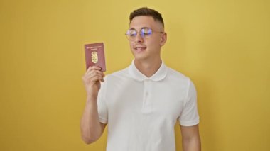 Neşeli, İspanyol asıllı genç adam Danimarka pasaportunu sevinçle sallıyor, kendine güvenen bir gülümsemeyle işaret ediyor. Dostça bir başarı ve onay jesti, parlak sarı arka planda izole edilmiş.