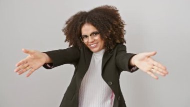 Parlak kıvırcık saçlı İspanyol kadın, izole edilmiş beyaz bir arkaplan önünde kollarını açıp kameraya doğru mutluluğu işaret ediyor.