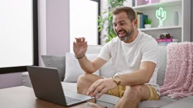 Sıradan bir ev ortamında gülümseyen orta yaşlı bir adam laptopuyla video görüşmesi yapıyor, rahat ve dostane bir atmosfer yayıyor..