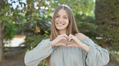Neşeli genç bir kadın, elleri yemyeşil bir bahçede bir kalp oluşturur. Olumlu ve sıcak bir hava yayar..