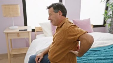 Sırtı ağrıyan olgun bir adam yatak odasında oturmuş huzursuzluk ve tedirginlik gösteriyor..