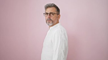 İzole edilmiş pembe arka planda sürpriz bir ifadeyle duran Latin kökenli gri saçlı genç adam.