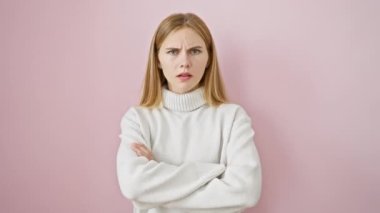 Yüzünde tasvip etmeyen bir ifadeyle güzel, kuşkucu sarışın kız, gergin bir şekilde kollarını pembe izole edilmiş arka planda kavuşturmuş - negatif titreşimler çoktur..
