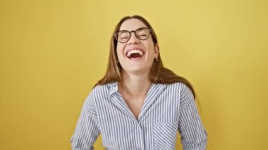 Mutluluktan uçuyor, genç bayan, gözlük takıyor! Eğlenceli mavi gözleri ışıldarken, komik bir fıkraya katıla katıla gülüyor sarı izole arka planda..