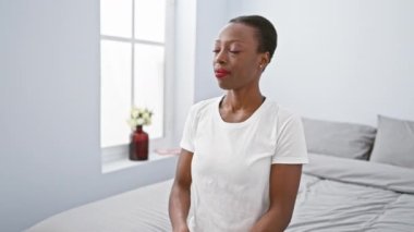 Afro-Amerikalı neşeli bir kadın yatak odasında dinleniyor, kendine güvenen bir gülümseme yayıyor, saf mutlulukla kendine sarılıyor ve kendini sevdiren olumlu bir jest yapıyor.