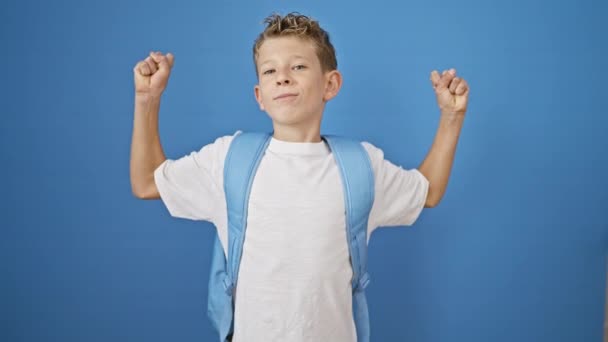 可爱的金发男生挥动着有力的臂膀 在孤独的蓝色背景下自信地微笑 这是童年学习的乐趣 — 图库视频影像
