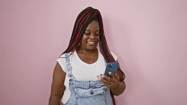 アフリカ系アメリカ人女性は ピンクの孤立した背景に電話でドル紙幣を欠いている オンライン賭けの勝者 — ストック動画