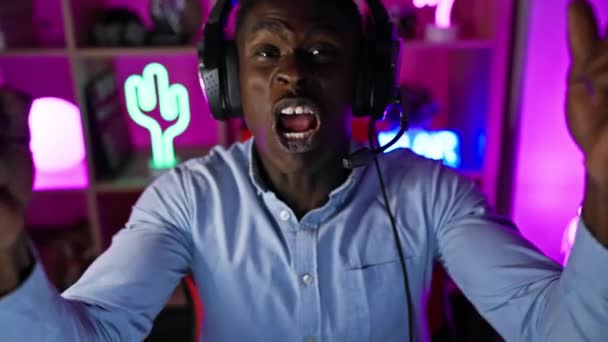 一个戴着耳机的兴奋的黑人男子在一个充满活力的游戏室庆祝胜利 — 图库视频影像