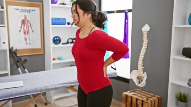 Hispanic Woman Experiencing Back Pain Rehab Clinic Interior Anatomical Charts — Stock Video