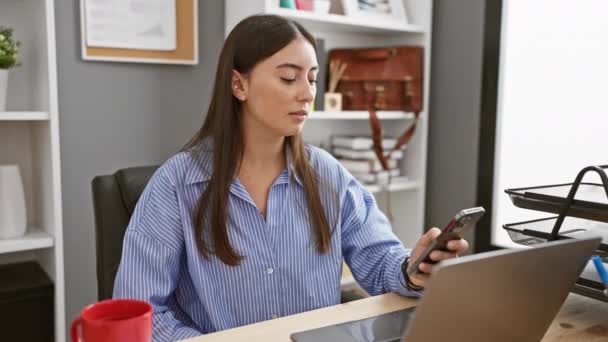 在现代办公环境中 西班牙女性在使用笔记本电脑时使用智能手机 — 图库视频影像