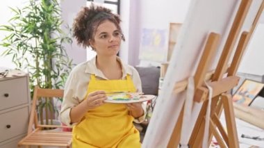 Parlak gözlü, kıvırcık saçlı İspanyol kadın sanatçı sevinçle oturur, stüdyosunu arar, elini kaldırır, mutlu bir bakışla uzaklara bakar..