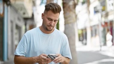 Sakallı genç bir adam bir şehir caddesinde akıllı bir telefon tutuyor, şehir yaşam tarzını yansıtıyor..