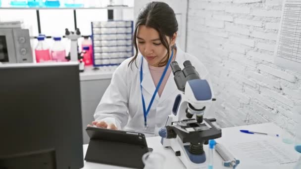 現代の実験室でタブレットと顕微鏡を使用したヒスパニック女性科学者 — ストック動画