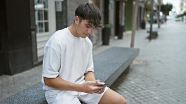 Heyecanlı İspanyol genç, kazanan, cep telefonunu kullanarak bir şehir caddesinde kutlama yapıyor, dışarıda neşeli bir mesaj yolluyor..