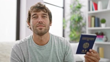 Mutlu genç adam, oturma odasındaki kanepesinde oturuyor, gülümsüyor, pasaportunu tutuyor, Kore 'ye yapacağı gezi için heyecanlanıyor.