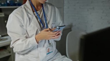 Beyaz önlüklü odaklanmış bir kadın bilim adamı modern bir laboratuvar ortamında akıllı telefon kullanıyor..