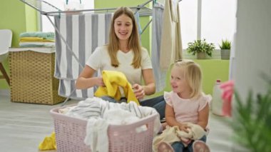 Kafkasyalı mutlu anne ve kız ev işleri üzerinde kaynaşıyor, çamaşır odasında yerde birlikte oturuyor, bir sepet dolusu kıyafet tutuyorlar.