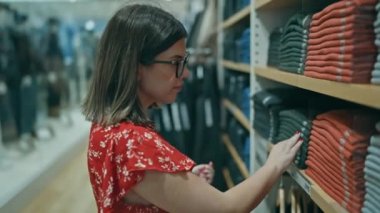 Moda tutkusu! Gözlüklü güzel İspanyol kadın perakende mağazasından şık kıyafetler seçiyor. Alışveriş merkezindeki bir butikten alışveriş yapan esmer bir kızın portresi..