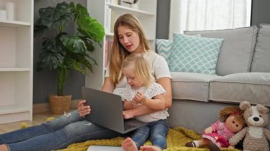 Evde, rahat bir beyaz anne ve kız dizüstü bilgisayarında bir filme dalmış, oturma odasında rahat bir şekilde oturuyorlar..