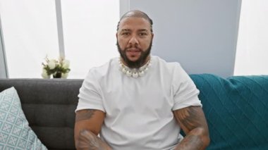 Heyecanlı Afrikalı Amerikalı adam zafer çığlıkları atıyor. Oturma odasındaki kanepede oturmuş zaferi kutlarken mutluluk ve kendine güven yayıyor. Kollarını kaldırarak başarıyı kutluyor..