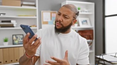Modern bir ofiste akıllı telefon kullanan, sakallı, kendinden emin, Afro-Amerikan bir adam..