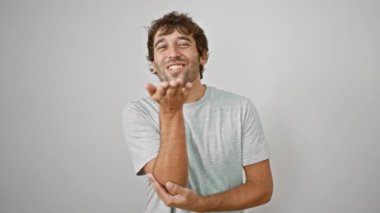 Yakışıklı genç adam kameraya sevgi dolu bir öpücük yolluyor, beyaz bir arka planda tek başına duruyor, sıradan bir tişört giyiyor.