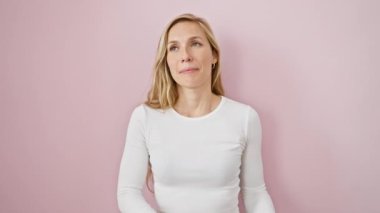 Neşeli genç sarışın kadın saf neşe saçıyor. Minnettar bir jestle elleri kalbinin üstünde duruyor. Pembe arka plan, parlayan sağlığını, mutluluğunu ve kendine güvenen gülümsemesini ortaya koyuyor..