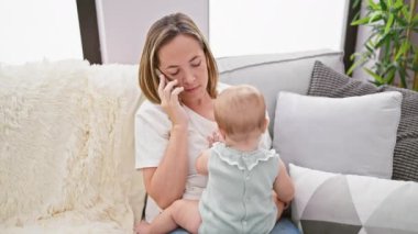 Anne akıllı telefonda konuşuyor, evde kızıyla koltukta oturuyor.