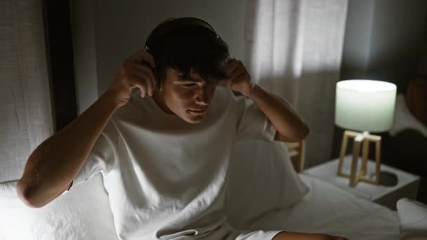 英俊而惊慌失措的少年欣赏着他最喜欢的歌曲 在舒适的卧室里悠闲自在地躺在舒适的床上 在昏暗的灯光下 — 图库视频影像