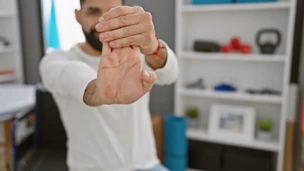 リハビリクリニックの職場で屋内で指を伸ばす若いヒスパニック男性 — ストック動画