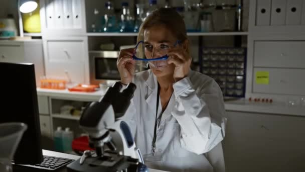一位戴安全眼镜的成熟女科学家在实验室的显微镜下工作 体现了专业精神和专注 — 图库视频影像